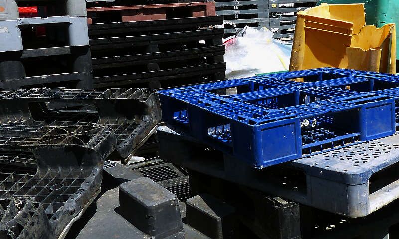 Ordentlich gestapelte schwarze und bunte Kunststoffpaletten lagern auf dem Firmengelände eines Recyclingunternehmens. Sie warten auf ihre Weiterverarbeitung und Wiedereinführung in den Rohstoffkreislauf als wertvoller sekundären Kunststoffrohstoff.