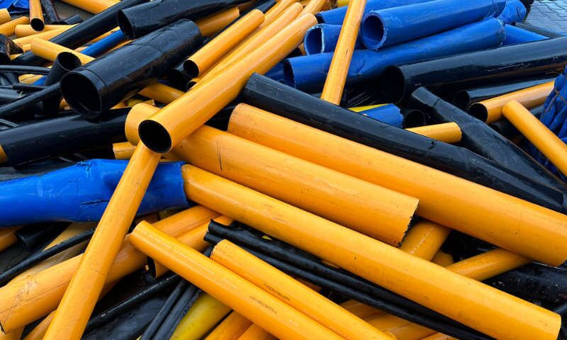 Schwarze, gelbe und blaue Kunststoffrohre aus HDPE, PA, PE, PP und PVC unterschiedlicher Durchmesser liegen ungeordnet auf einem Haufen. Abfall aus Kunststoffrohren wird sortiert, gemahlen, gewaschen, zu Mahlgut verarbeitet und transportfähig abgefüllt.