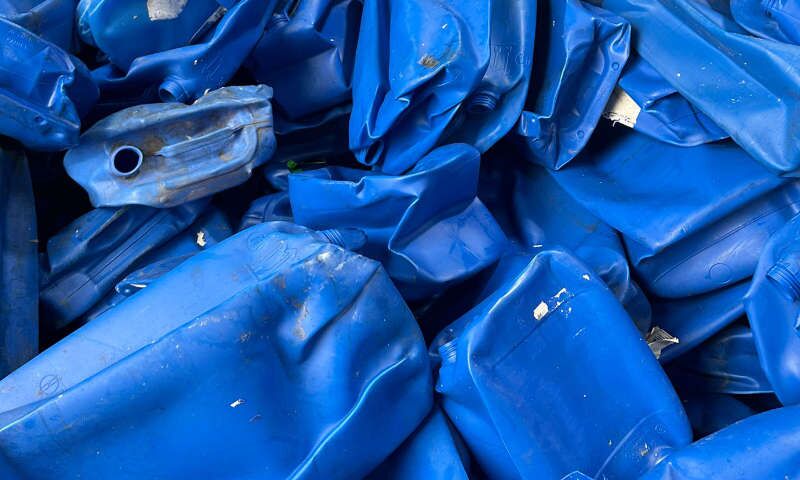 Wertvoller Sekundärrohstoff im Antlitz ausgedienter blauer Plastikkanister liegt zu einer Farbe sortiert auf dem Gelände eines Recyclingunternehmens. Manche der Kunststoffkanister sind eingedrückt, andere geplatzt oder zerquetscht.