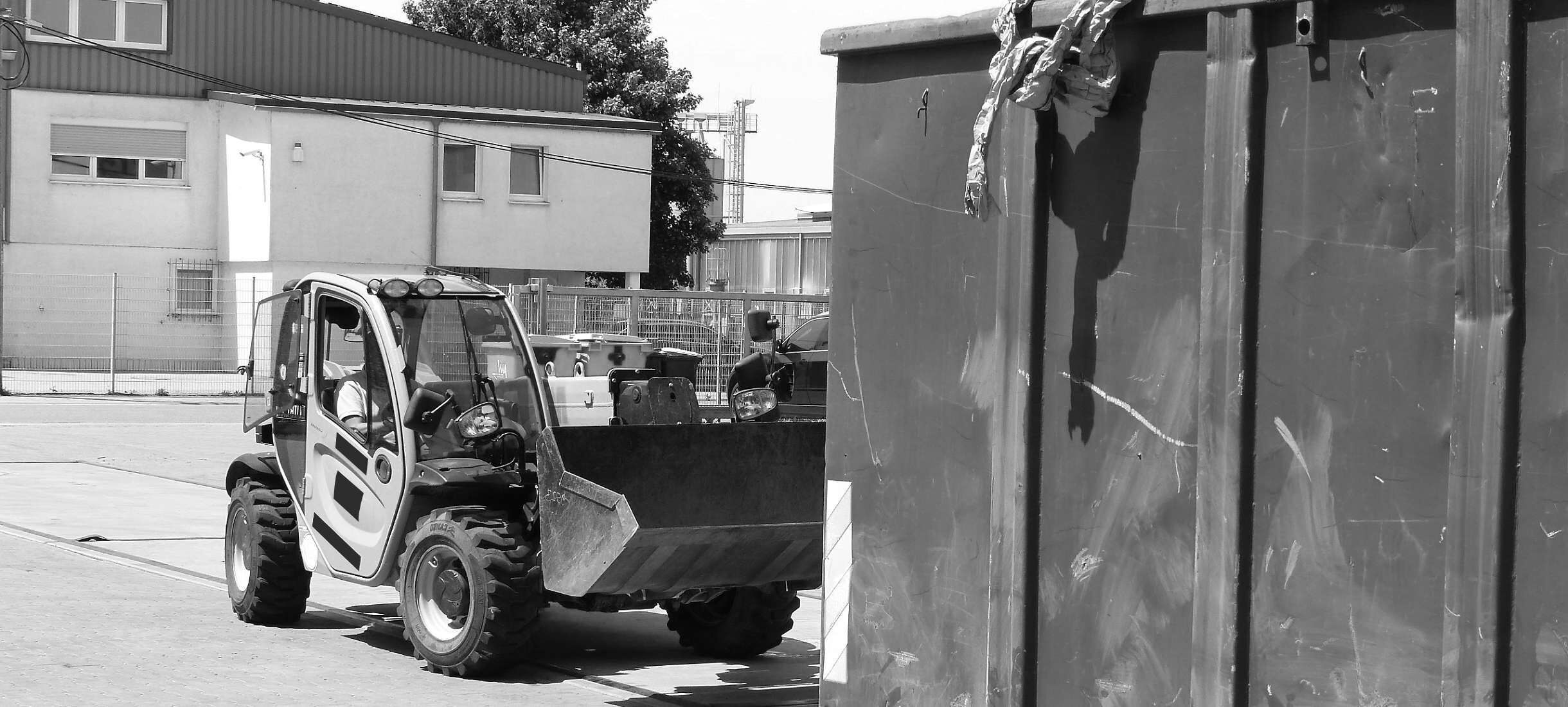 Großcontainer wird mit Kunststoff- und Plastikresten befüllt. Mitarbeiter des Recyclingunternehmens entlädt Plastikabfall in den Container für wiederverwertbaren Rohstoff mit einem Radlader auf vier Rädern. Plastik ragt aus dem Abfallcontainer.