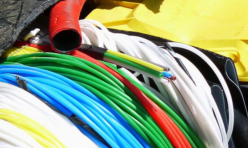 Bunte Stränge unterschiedlicher, mit Kunststoff isolierter Internetkabel zu mehreren Ringen aufgerollt. Der Kunststoffdeckel einer Plastiktonne für Plastikabfall. Entsorgte Kunststoffe lagern bevor sie in Rohstoffkreislauf zurückgeführt werden.