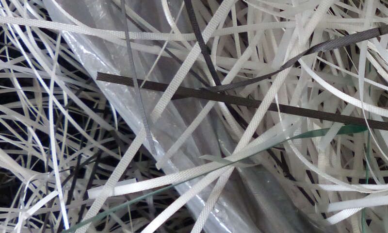 Weißes und schwarzes Kunststoff-Umreifungsband, Kabelbinder aus Polypropylen liegen sortiert in und außerhalb einer Plastiktüte. Dieser entsorgte Plastikabfall wird recycelt und als Kunststoff-Sekundärrohstoff in den Rohstoffkreislauf zurückgeführt.