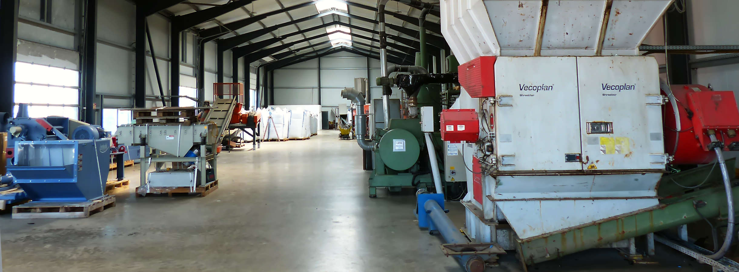 Große helle Produktionshalle der Xpress Plastics GmbH für Plastik-Recycling. An den Seiten große Maschinen zum sortieren, schreddern, mahlen, waschen von Kunststoffabfällen. Am Hallenende stehen mit aufbereitetem Kunststoffmahlgut abgefüllte Big Bags.