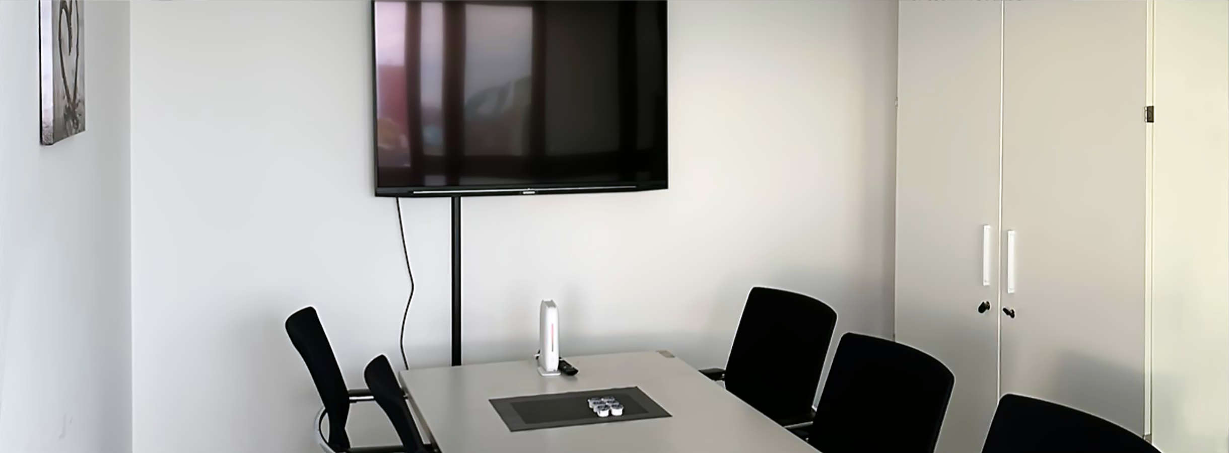 Meeting-Raum des Recyclingunternehmens Xpress Plastics für Team- und Strategie-Besprechungen. Ein langer weißer Tisch steht mitten im Raum. An beiden Seiten stehen schwarze Stühle. Ein großer Flachbildschirm hängt an der Wand über dem Tischende.