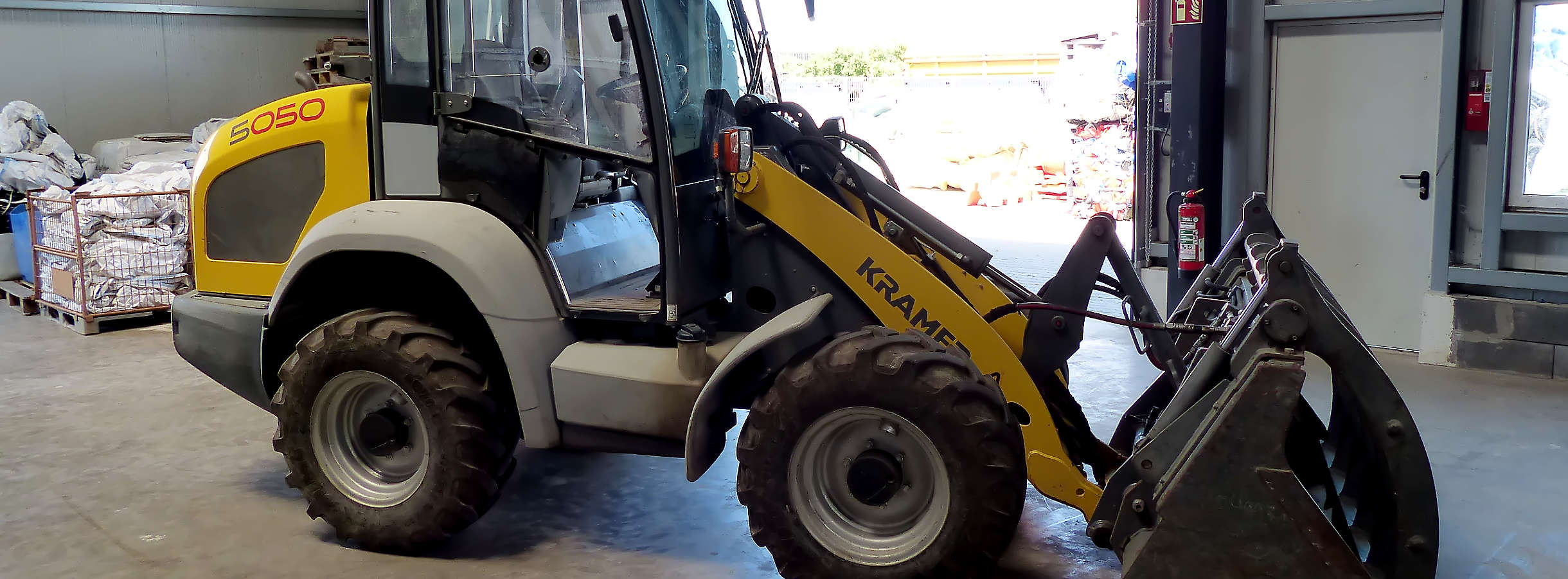 In der Halle für Plastik- und Kunststoffrecycling der Xpress Plastics GmbH in Biebesheim am Rhein steht ein gelber Radlader. Im Hintergrund liegen leere Big Bags auf einer Palette. Sie werden mit Mahlgut aus recyceltem Kunststoffabfall befüllt.