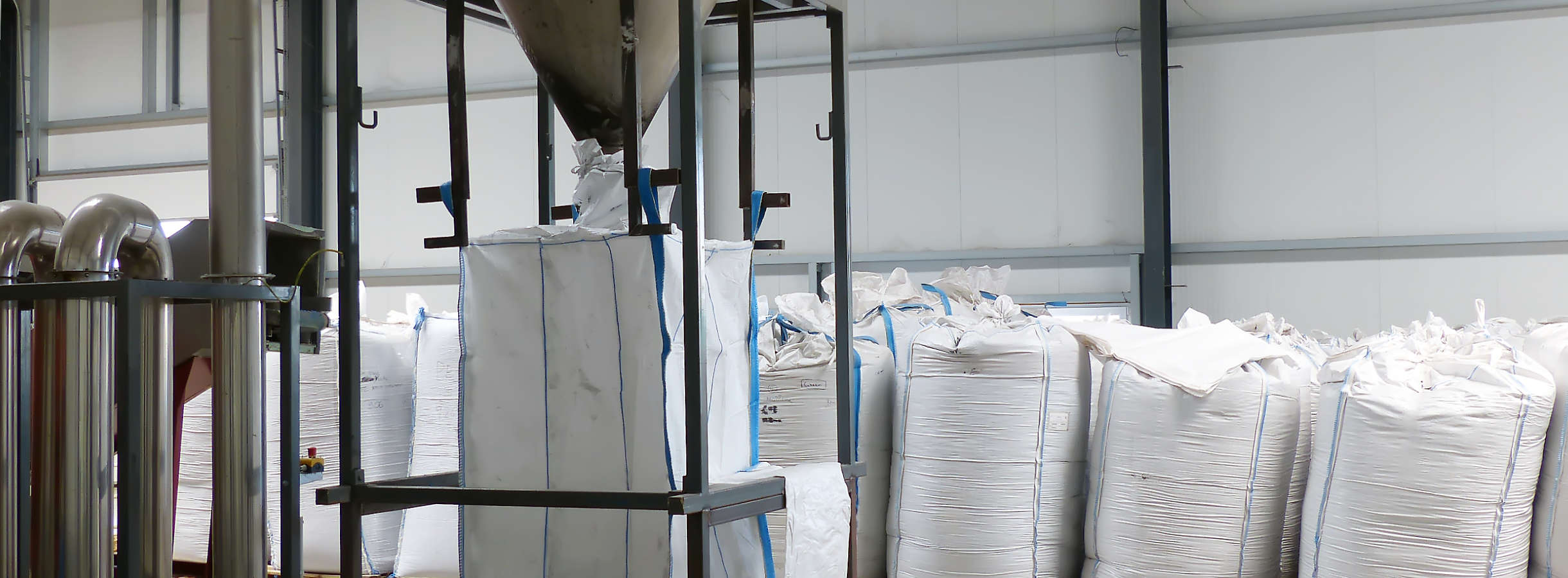 In der Halle vom Entsorgungsfachbetrieb stehen Big Bags mit abgeholten, dokumentierten und zu Kunststoff-Mahlgut verarbeiteten Kunststoffabfall. Absackanlage füllt einen Weiteren mit recycelten Plastik für den Handel, Rückführung in den Rohstoffkreislauf.