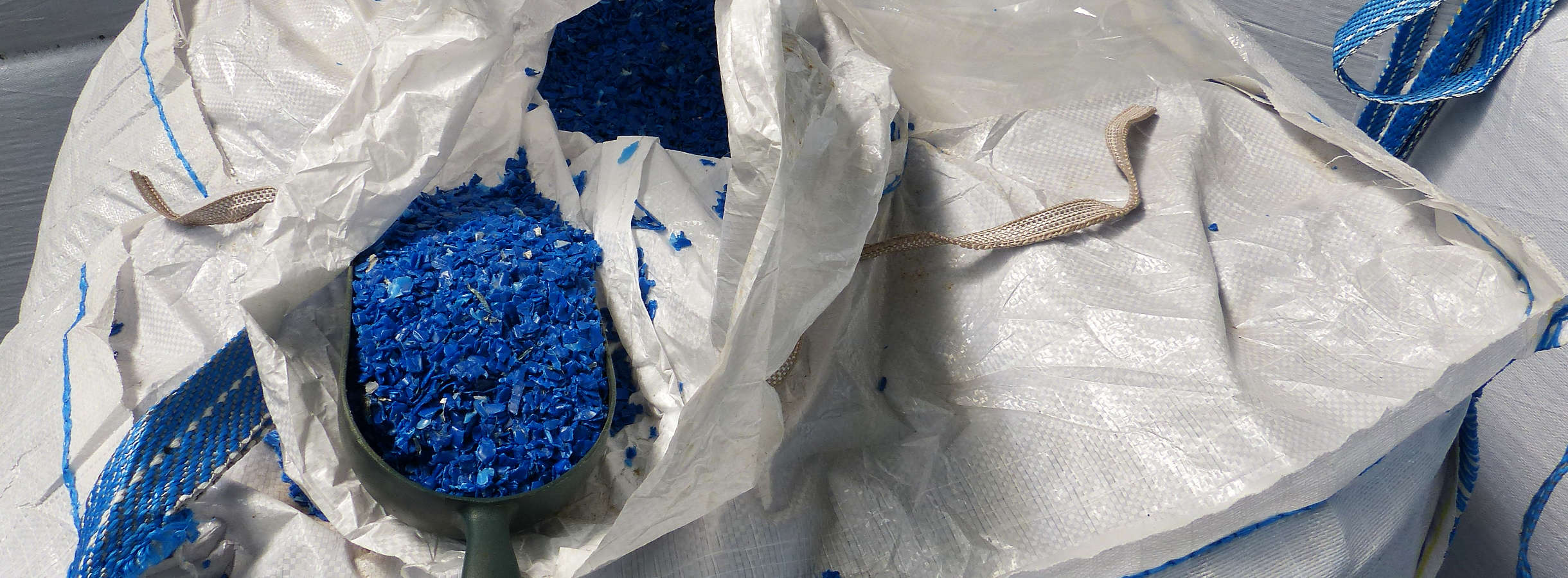 Hochwertiges PE 100-Mahlgut, aus Vollwand-Druckrohren recycelt, füllt eine Schöpfkelle in den Hallen der Entsorgungsfirma Xpress Plastics in Bibesheim am Rhein. Die Kelle liegt auf einem riesigen weißen Sack des aufbereiteten Sekundärrohstoffes.