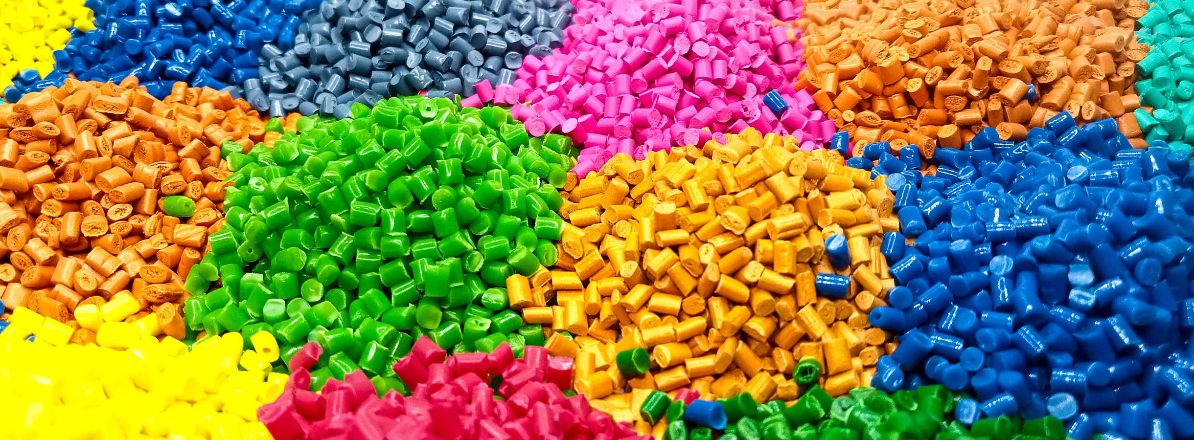 Verschiedenfarbige hochwertige Kunststoff-Granulate, wie PP-Granulate, PE-Granulate oder Granulat aus recycelten technischen Kunststoffen sind zu kleinen Häufchen gestapelt. Die Lagerfläche befindet sich in der Firma für Plastics Recycling Management.