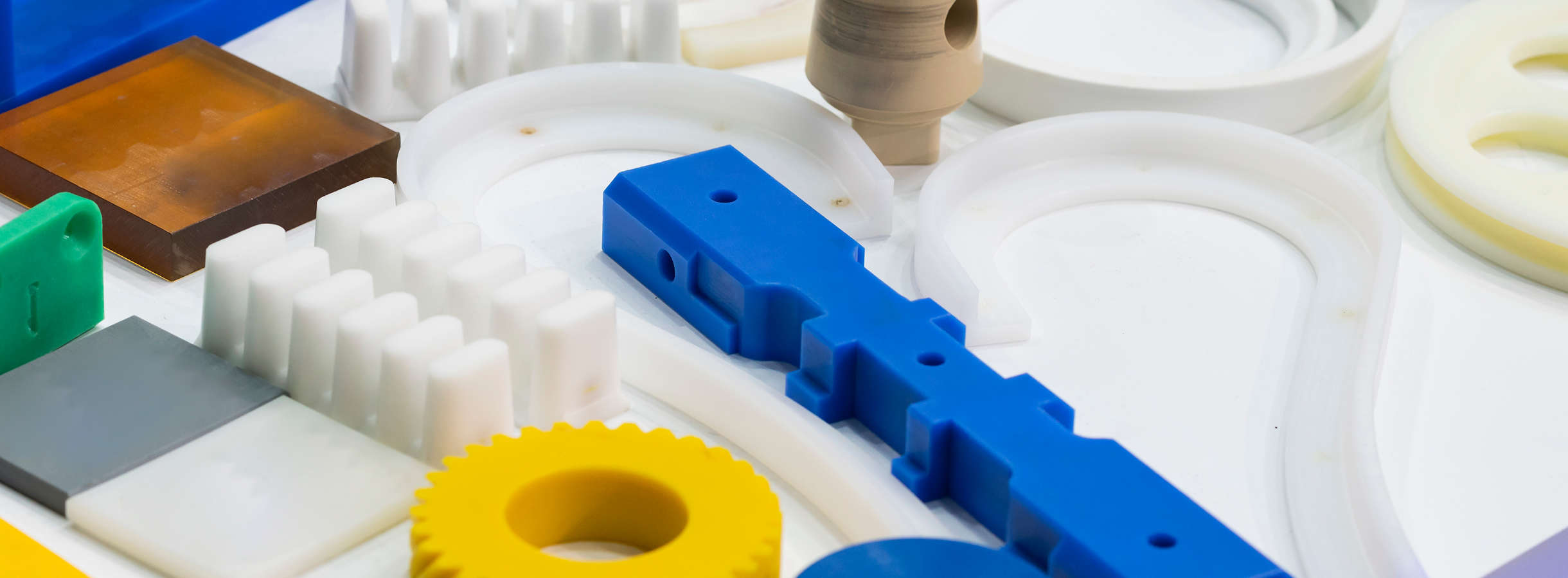 Unterschiedliche Technische Kunststoffe wie PA, PC, ABS, POM und weitere thermoplastische Hochleistungspolymere liegen auf einer weißen Tischoberfläche. Kunststoffe mit außergewöhnlichen, mechanischen, thermischen und chemischen Eigenschaften sind bunt.