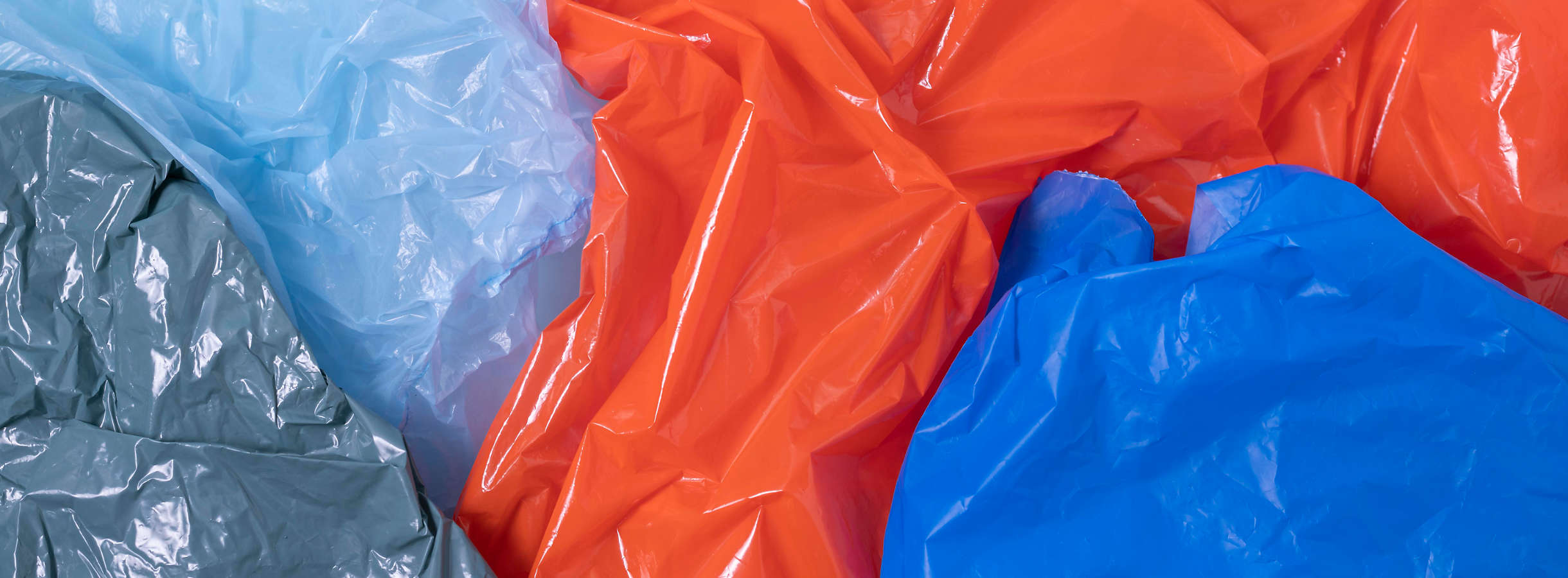 Verschiedenfarbige Plastikfolien spiegeln das Licht der Produktionshalle vom Xpress Plastics Entsorgungsunternehmen. Graue Plastikfolie, hell- und dunkelbaue Plastikfolie, eine rote Plastikfolie werden recycelt und als Rohstoff verkauft.